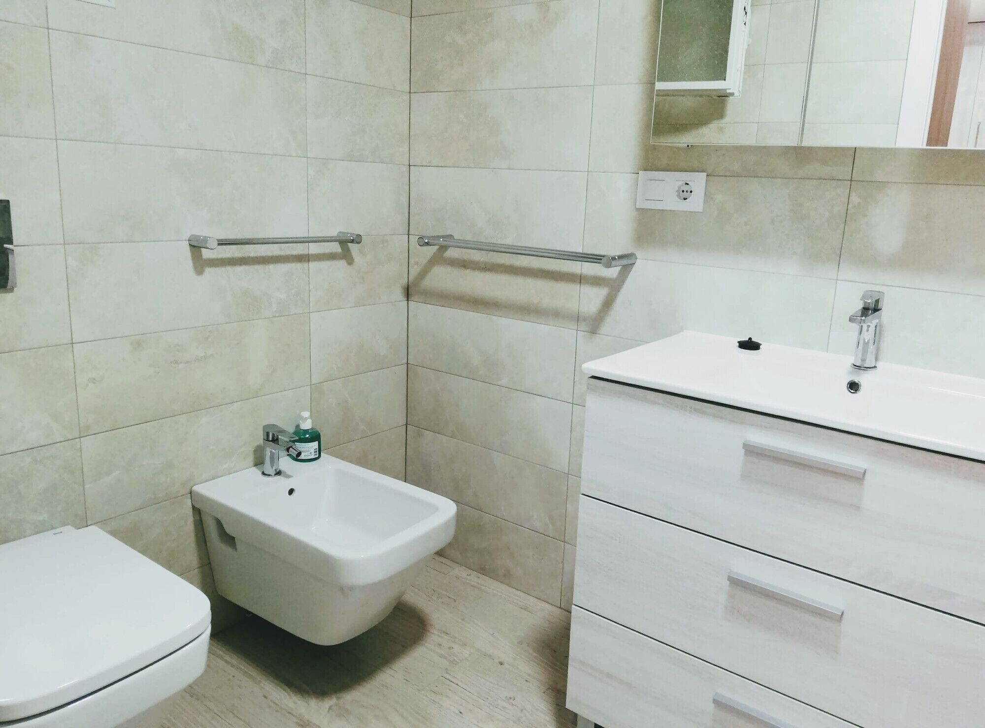 Un baño con inodoro, bidé, tocador con lavamanos y espejo.
