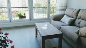 Un soggiorno con un divano, un tavolino in legno e un'ampia finestra vista un balcone e degli edifici.