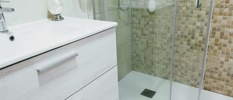 A modern bathroom with a white vanity, a glass shower enclosure, and a tiled shower wall.