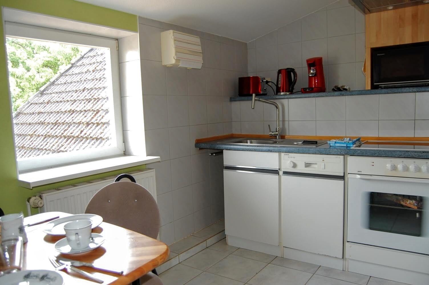 Een compacte keuken met witte apparatuur, een raam en uitzicht op het dak.