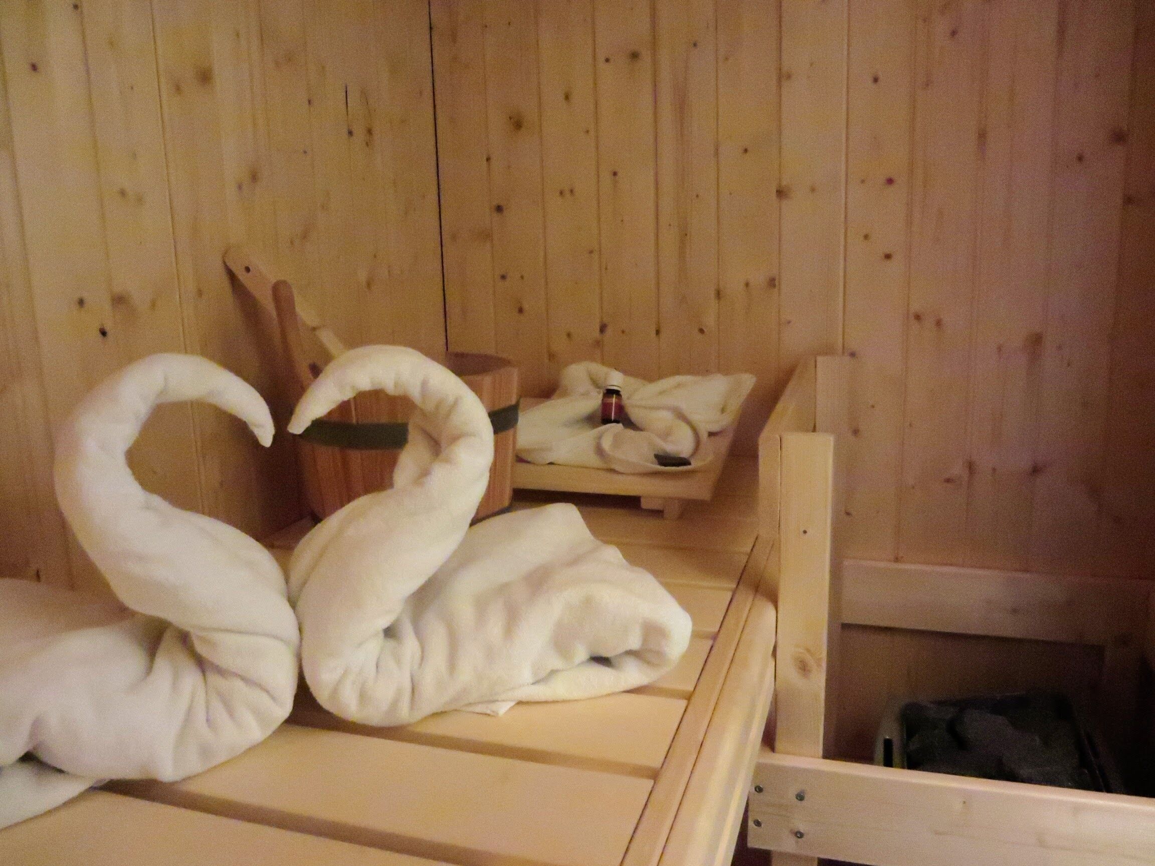 A wooden sauna room with two swan-shaped towels on a bench.