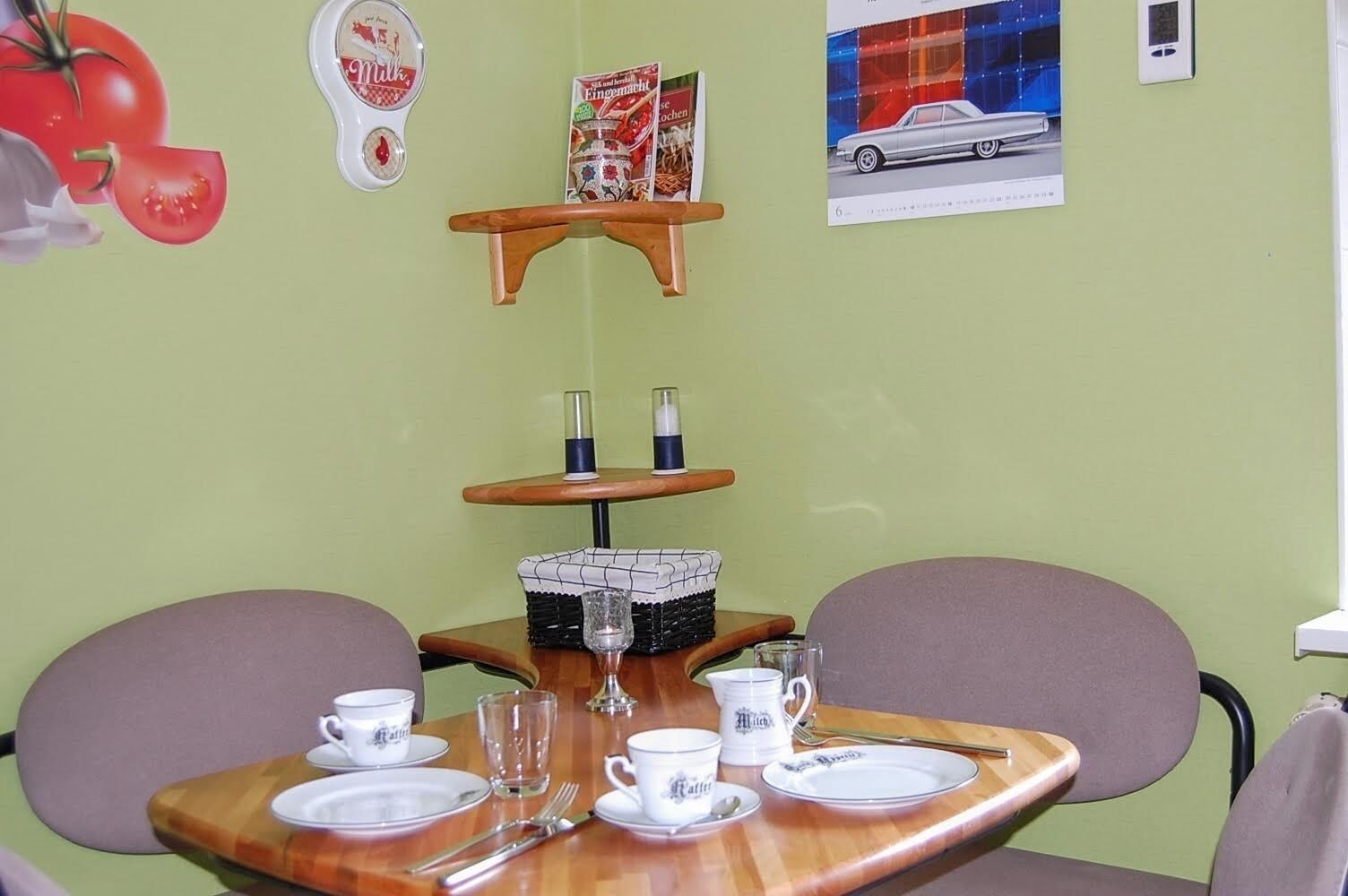 Un'area pranzo con un tavolo di legno apparecchiato per due, un piccolo ripiano con una confezione di latte e una rivista appesa al muro.