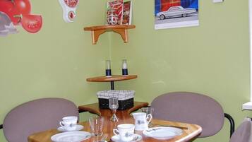 Un'area pranzo con un tavolo di legno apparecchiato per due, un piccolo ripiano con una confezione di latte e una rivista appesa al muro.