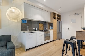 Enjoy cooking and dining in this stylish kitchen with sleek cabinetry, a wooden shelf, and pendant light.