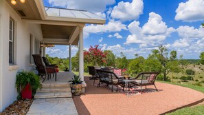 Une terrasse couverte, aménagée avec du mobilier d’extérieur, un chemin en pierre et une vue sur le paysage environnant.