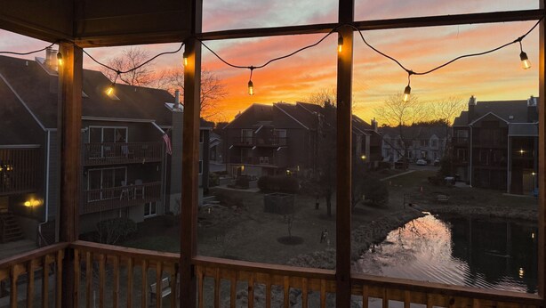 Uitzicht vanaf een balkon met houten leuning, over een woongebied met huizen en een klein waterpartij.