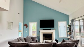 Een woonkamer met een blauwgroene wand, een open haard, een flatscreen televisie en een groot raam.