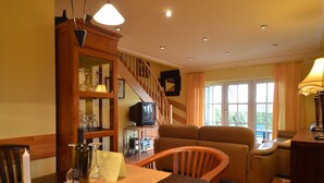 A cozy living room with a wooden staircase, a television, and a dining area with a table set for two.