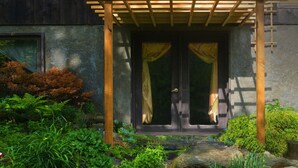 Una pérgola de madera sobre una entrada de piedra con cortinas, rodeada de exuberante follaje y rocas.