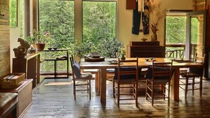 Un comedor rústico con muebles de madera, ventanas amplias que ofrecen vistas a la vegetación y una decoración sencilla y práctica.