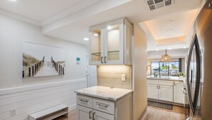 A modern kitchen with white cabinetry, a marble countertop, and a large window providing natural light. - Land's End 204 building 4 Premier|Large Pool|Steps to beach access! (Treasure Island)