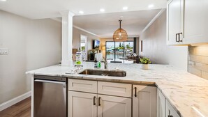 A modern kitchen with a dishwasher, sink, and white cabinets. - Land's End 204 building 4 Premier|Large Pool|Steps to beach access! (Treasure Island)