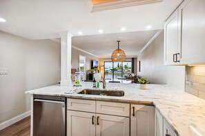 A modern kitchen with a dishwasher, sink, and white cabinets. - Land's End 204 building 4 Premier|Large Pool|Steps to beach access! (Treasure Island)