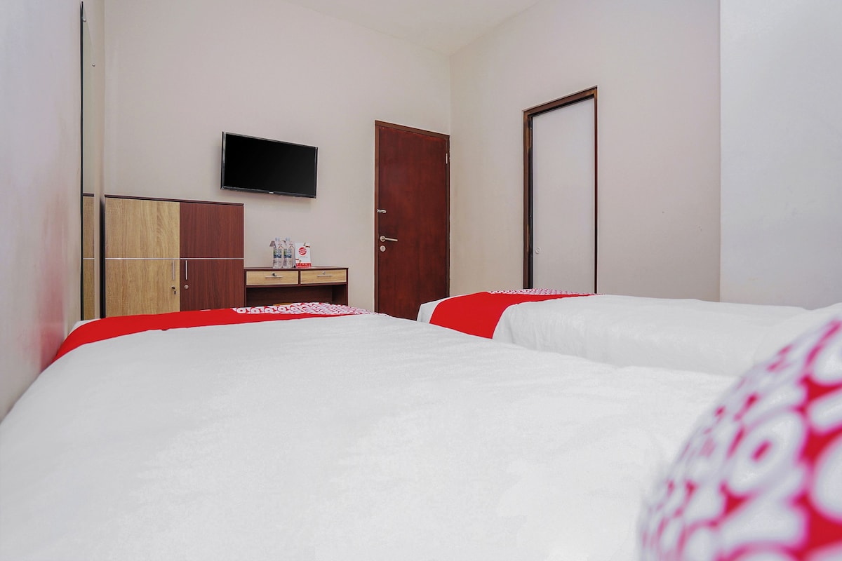 A hotel room with two beds, a TV mounted on the wall, a wooden wardrobe, and a door.