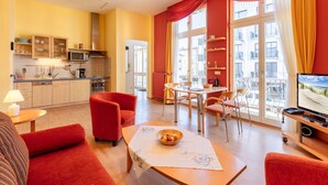 Un salon moderne avec un canapé rouge, une table à manger avec des chaises, un téléviseur et un coin cuisine équipé de placards et d’un four à micro-ondes.