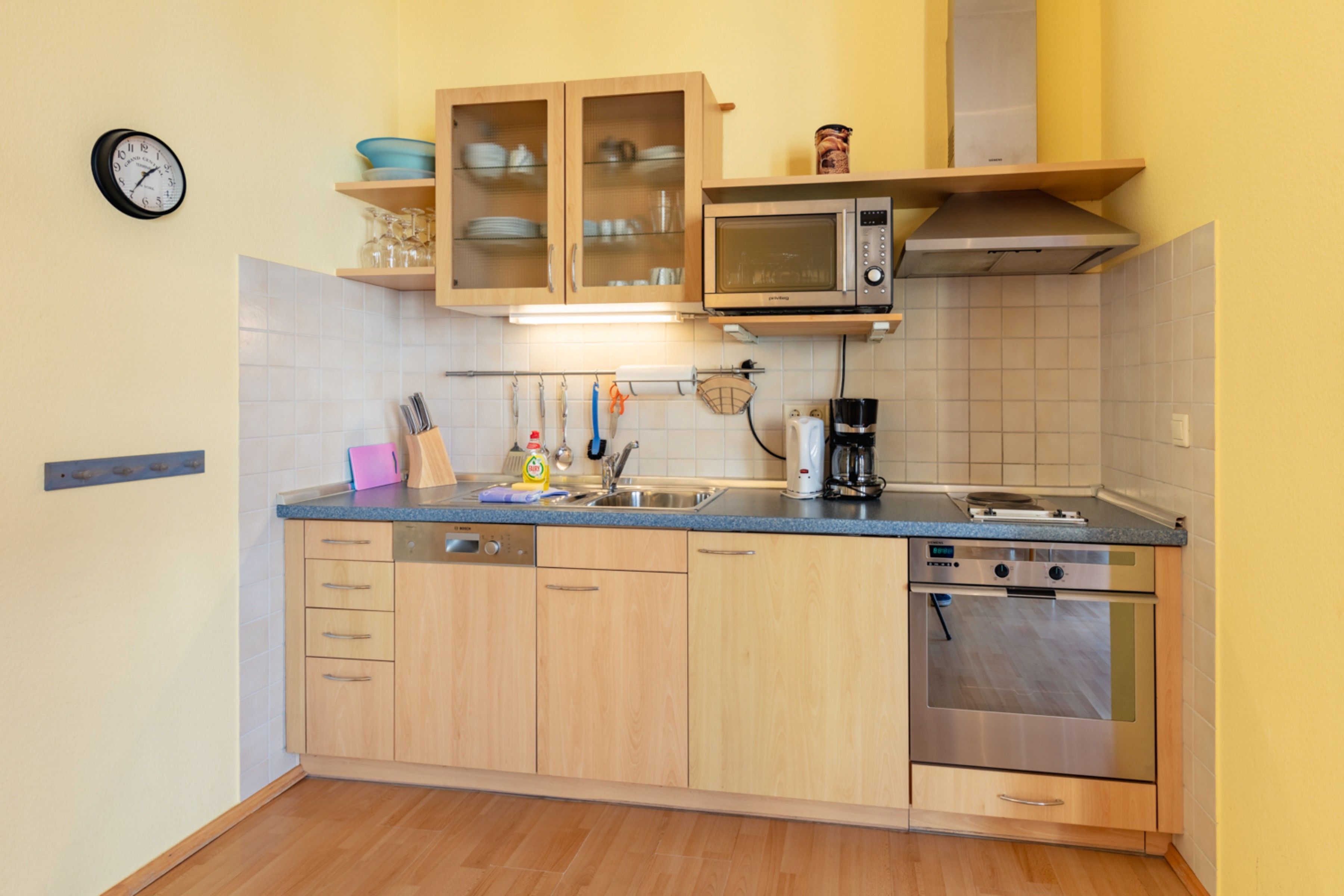 A kitchen with wooden cabinets, a microwave, a coffee maker, and a clock on the wall.