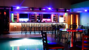 A bar area with wooden cabinets, a pool, and multiple seating arrangements. - Leisure Inn (New Amsterdam)