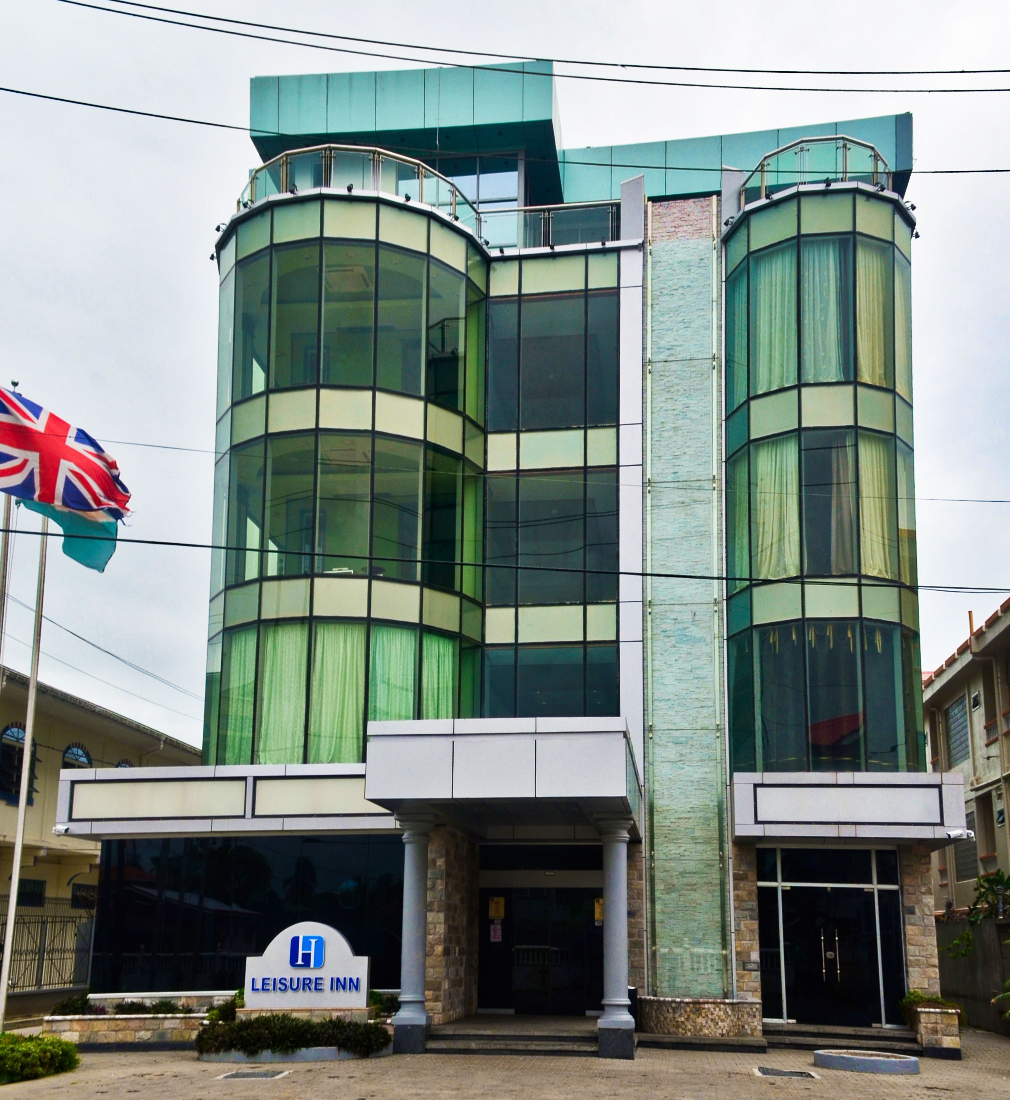A LEISURE INN building with a modern glass facade, a flag, and a signboard.