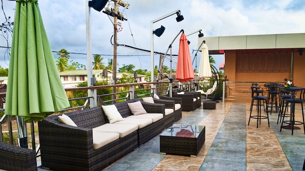 A rooftop patio with wicker sofas, a bar area, and umbrellas. - Leisure Inn (New Amsterdam)