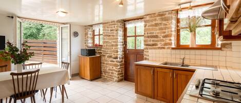 A kitchen with a stone wall, wooden cabinets, a tiled backsplash, a stove, and a dining area with a table and chairs.
