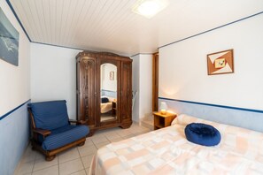 Un dormitorio con cama, una silla, un armario y una mesita de noche con lámpara.