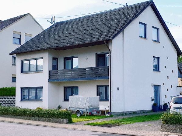 A two-story residential building with a balcony on the upper floor, a satellite dish, and a covered vehicle parked in front.