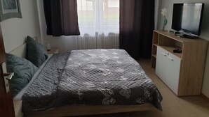 Quarto com cama, televisão sobre suporte de madeira e janela com cortinas.