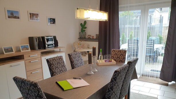 Uma sala de jantar com uma mesa posta para quatro pessoas, rodeada por cadeiras estampadas. Há uma máquina de café e uma pequena planta no balcão.