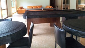 A pool table in a room with a wooden ceiling, a sofa with orange cushions, and a dining table with chairs. - 2 bedrooms, 1 suite, 2 bathrooms, 100 m from the best location in Praia da Baleia. (São Sebastião)