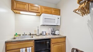 A compact kitchen with wooden cabinets, a built-in microwave, a coffee maker, and a dishwasher. - 107 Deluxe Studio Queen, w/ Sleeper sofa w/ outdoor heated pool (Killington)