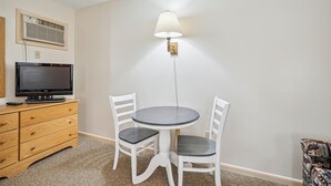 A small room with a round table and two chairs, a television on a wooden cabinet, and a wall-mounted lamp. - 107 Deluxe Studio Queen, w/ Sleeper sofa w/ outdoor heated pool (Killington)