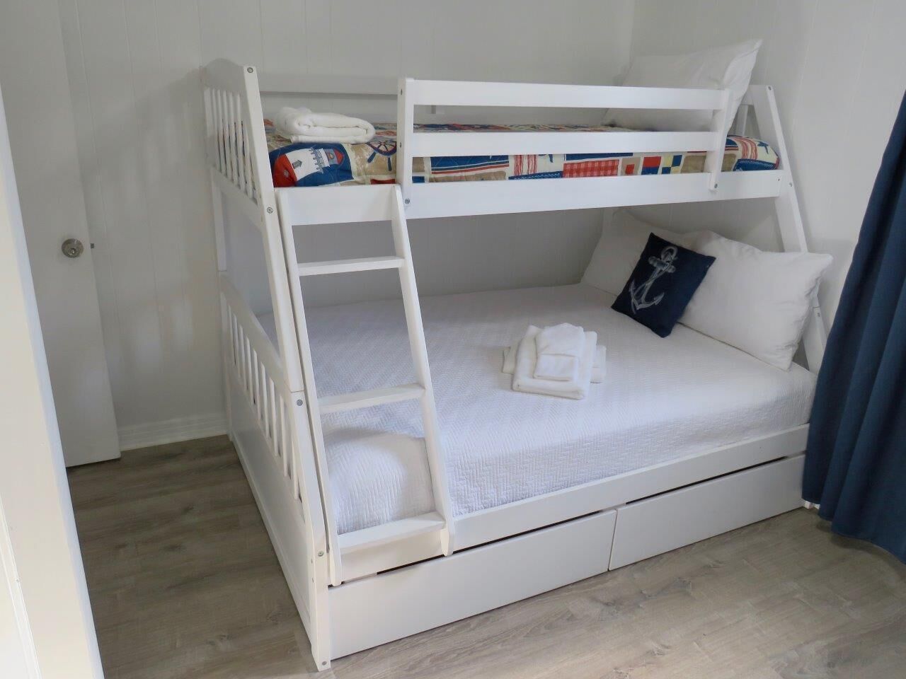 A bunk bed with a ladder, a pillow with an anchor design, and a folded towel on the lower bunk.