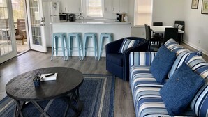 Una cocina moderna con armarios blancos, una zona de comedor con un sofá y sillas a rayas, y una mesa redonda con una planta.