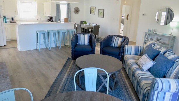 Una sala de estar moderna con un sofá, sillas, una mesa de centro y un comedor con taburetes.