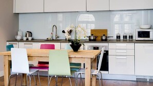 Une cuisine moderne avec des meubles blancs, une table à manger en bois et un vase rempli de fleurs.