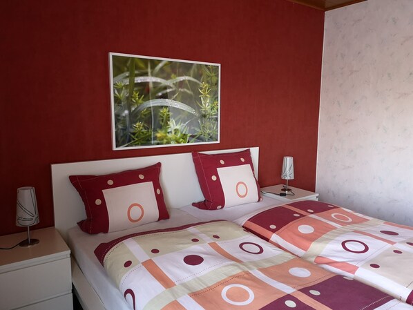 Une chambre à coucher avec un lit, deux tables de chevet, une lampe et une fenêtre donnant sur un paysage verdoyant.
