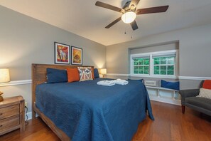 A bedroom with a large bed, a ceiling fan, a window with a view, and a bedside table.