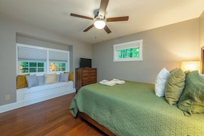 A bedroom with a bed, a window seat, a ceiling fan, and a dresser.