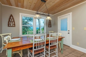 A dining area with a wooden table, white chairs, and a hanging light fixture. - Hot Tub+Fire Pit, Mtn Sunsets, Fireplace & Grill! (Spruce Pine)