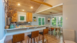 A kitchen with wooden bar stools, a large island, and a dining area with a table and chairs. - Sunset Mtn Lodge! Hot tub+Fire pit, Fireplace, Hiking, Private, Close to Town! (Spruce Pine)