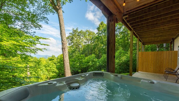 A hot tub in a wooded area with a wooden deck and chairs. - Sunset Mtn Lodge! Hot tub+Fire pit, Fireplace, Hiking, Private, Close to Town! (Spruce Pine)