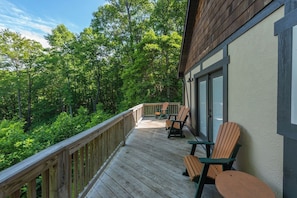 A wooden deck with outdoor seating, surrounded by lush greenery. - Hot Tub+Fire Pit, Mtn Sunsets, Fireplace & Grill! (Spruce Pine)