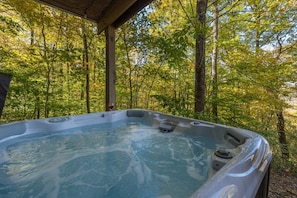 A hot tub in a forested area with a wooden structure overhead. - Hot Tub+Fire Pit, Mtn Sunsets, Fireplace & Grill! (Spruce Pine)