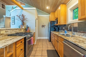 A kitchen with granite countertops, wooden cabinets, stainless steel appliances, and a view of the outdoors. - Hot Tub+Fire Pit, Mtn Sunsets, Fireplace & Grill! (Spruce Pine)