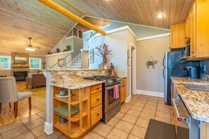A kitchen with a granite countertop, wooden cabinets, and a stainless steel refrigerator. - Hot Tub+Fire Pit, Mtn Sunsets, Fireplace & Grill! (Spruce Pine)