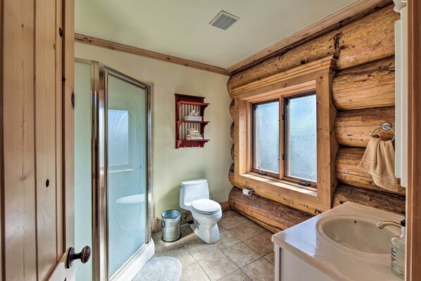Un baño con pared de tronco de madera, un inodoro, un lavamanos y una ventana.