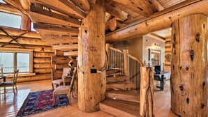 Interno di una baita di legno con una scala in legno, travi rustiche e un'ampia finestra.