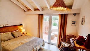 A bedroom with a bed, a nightstand with a lamp, a chair, and a view through a glass door to an outdoor area. - Guest Room in nature in Minorca : Adults Only  (Ferreries)