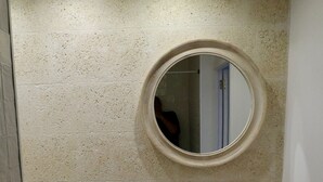 A bathroom with a round mirror, a white sink, a wooden shelf, and a woven basket. - Guest Room in nature in Minorca : Adults Only  (Ferreries)