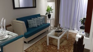 A living room with a blue sofa, a coffee table, a plant, and a dining area with a table set for two. - Affordable Luxury 2BR Condo in Davao City (Davao City)